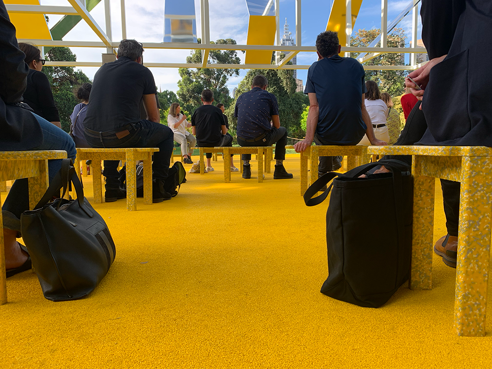 A photo of a bright yellow floor during a panel talk, showing crowd members listening intently